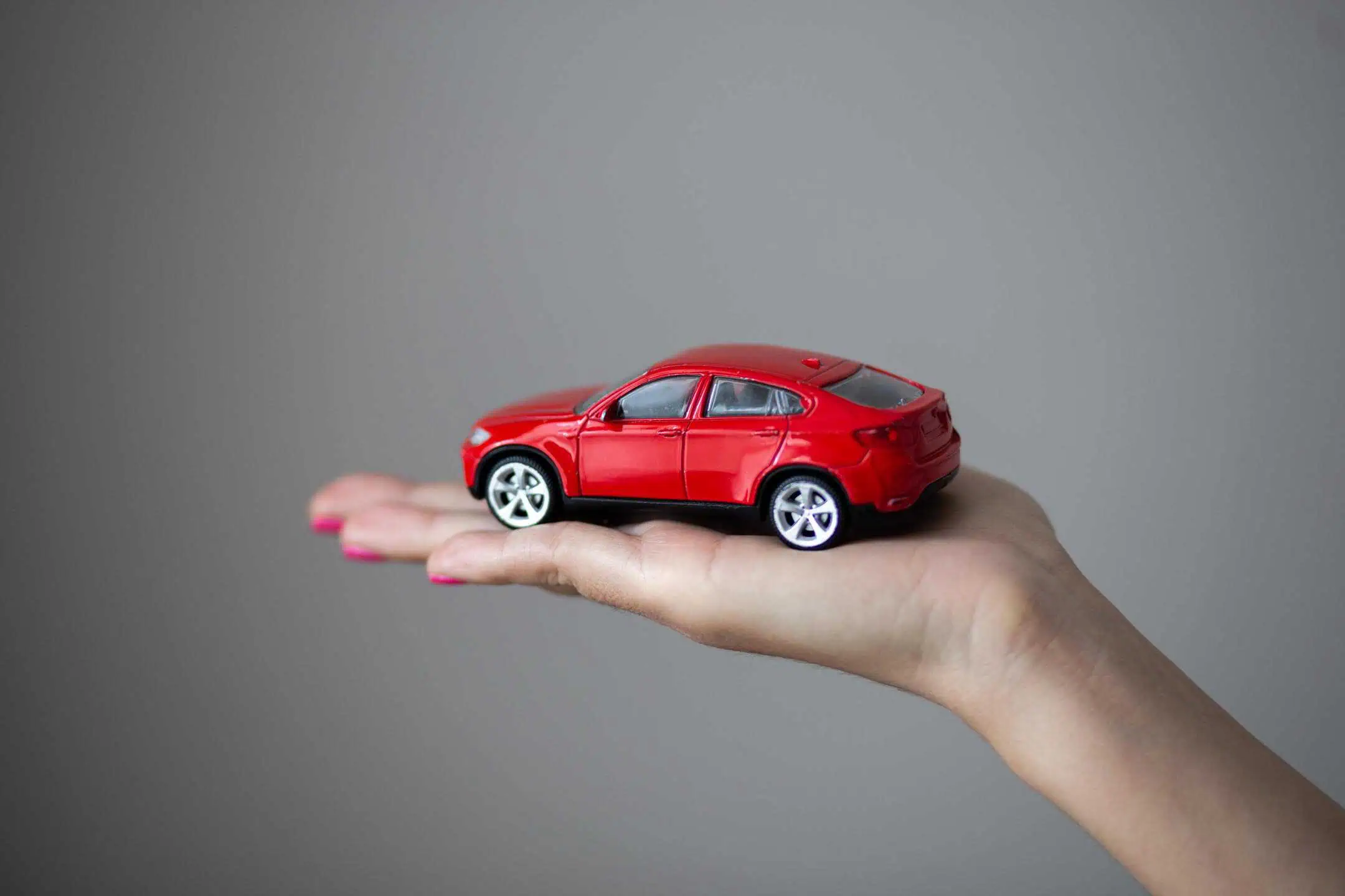 Hand Holding Toy Car In Palm Grey Background