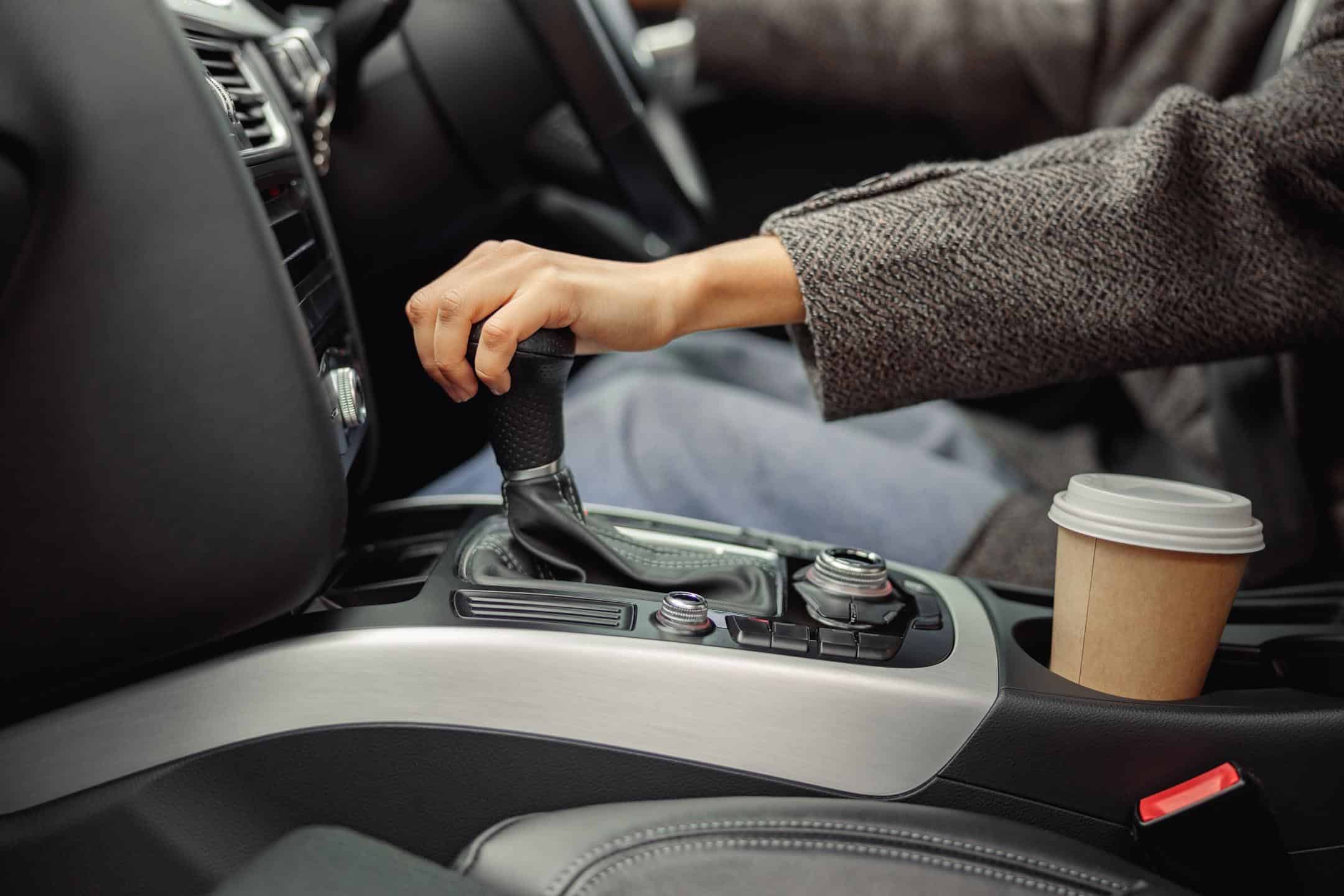 Hand On Gear Stick With Coffee Cup In Holder