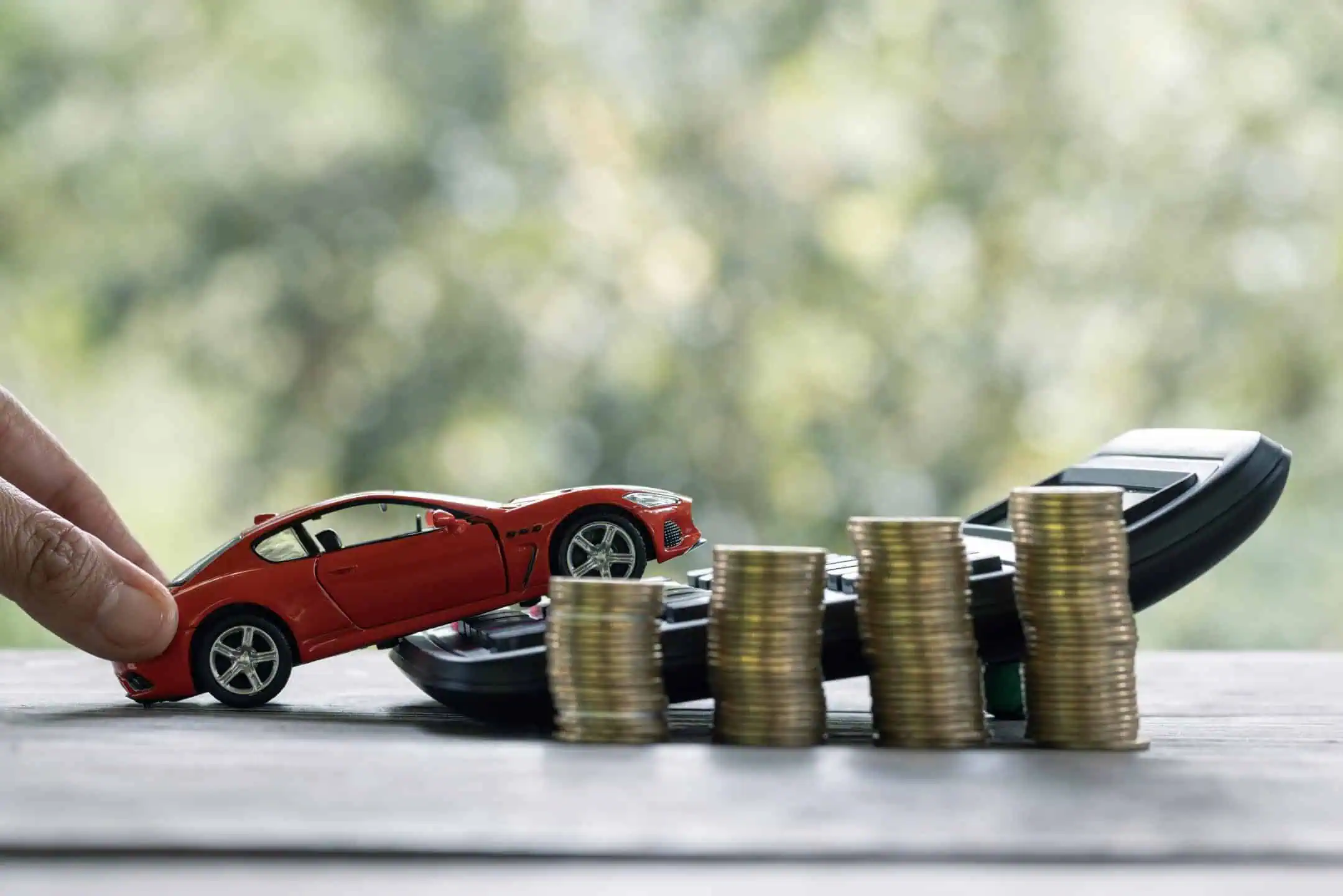 Man Pushing Red Toy Car Over A Calculator With Coins