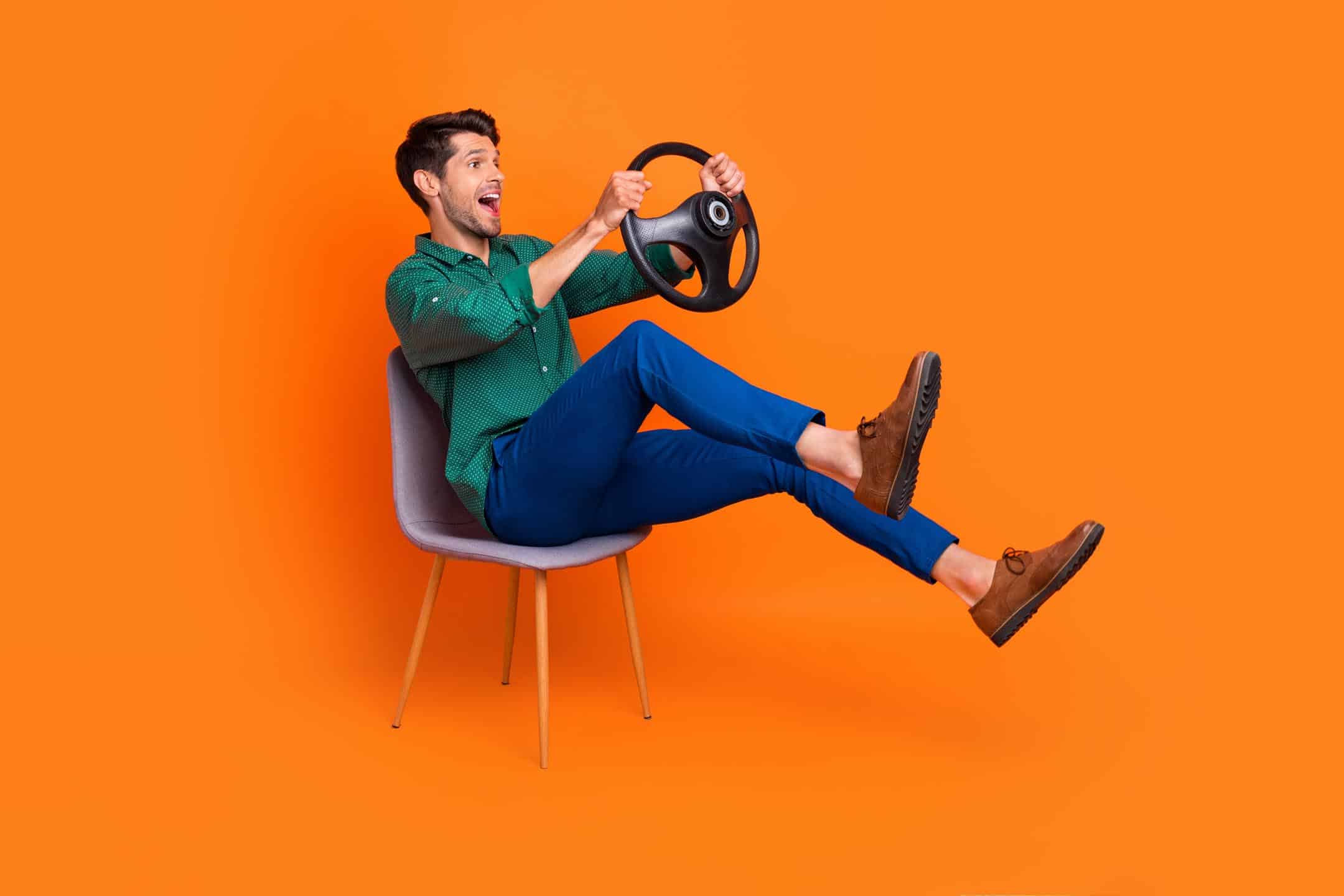 Man Sitting Down Holding Steering Wheel With Orange Background