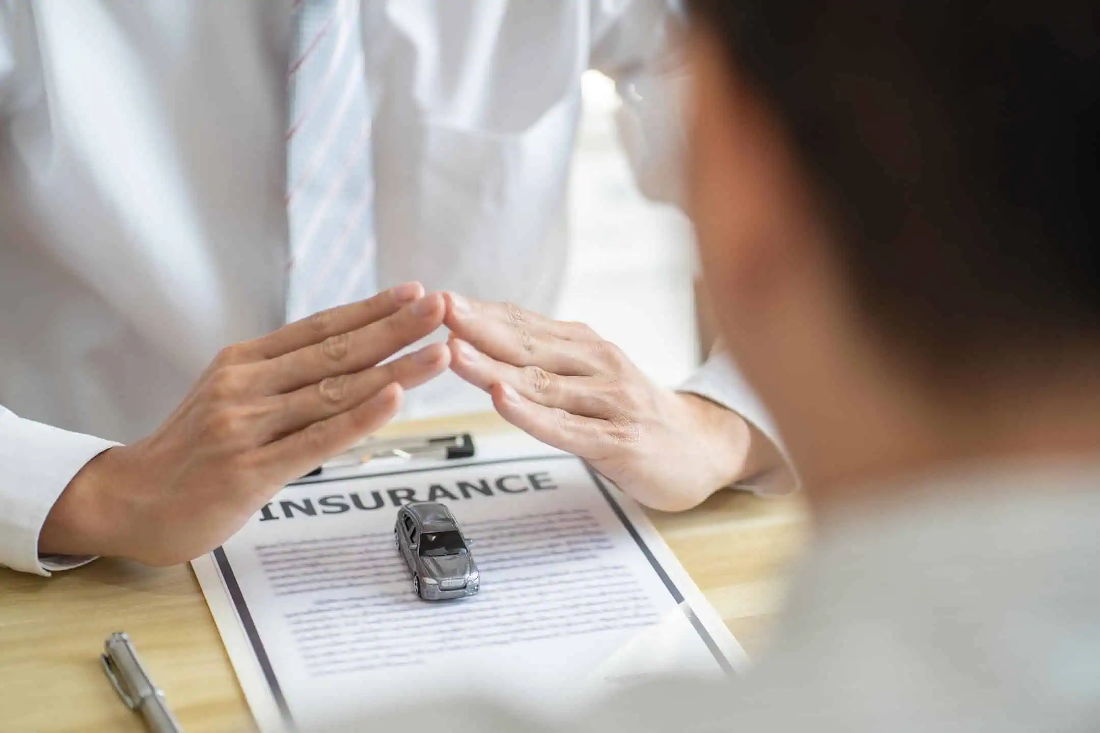 Man With Hands Covering Toy Car On Insurance Document